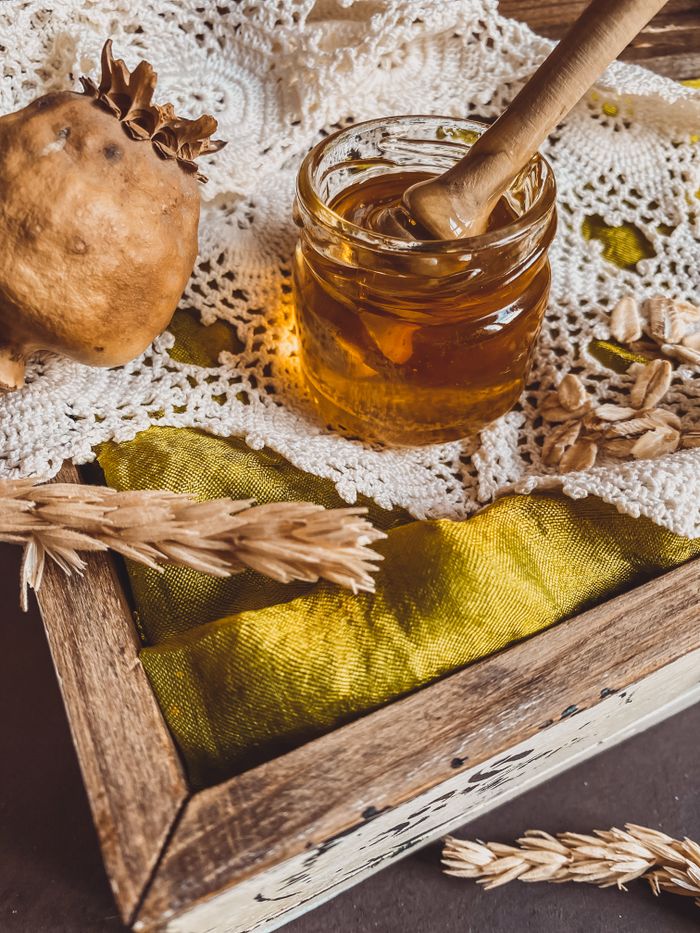 Close-up of a honey jar with dipper on lace fabric in a rustic Turkish setting.