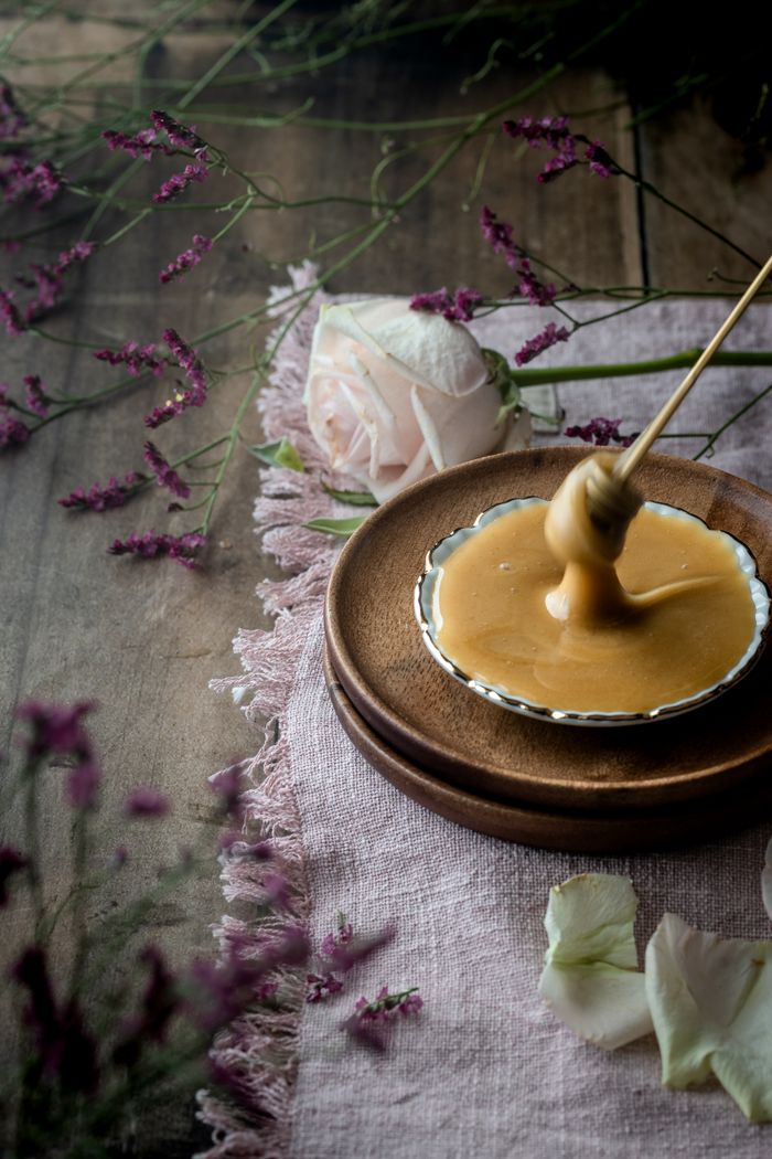 Aesthetic honey drizzle with a pink rose and petals on a rustic wooden table.